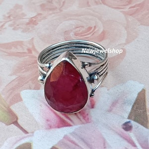 May include: A silver ring with a large, teardrop-shaped ruby gemstone. The ring has a delicate, multi-layered band.