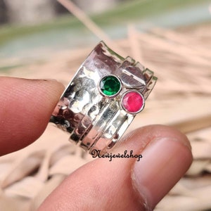 May include: A silver spinning ring with a green and red gemstone. The ring is hammered and has a textured surface.