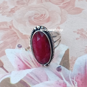 May include: A silver ring with a large, oval-shaped, red gemstone set in a decorative, beaded bezel. The ring has a twisted band.