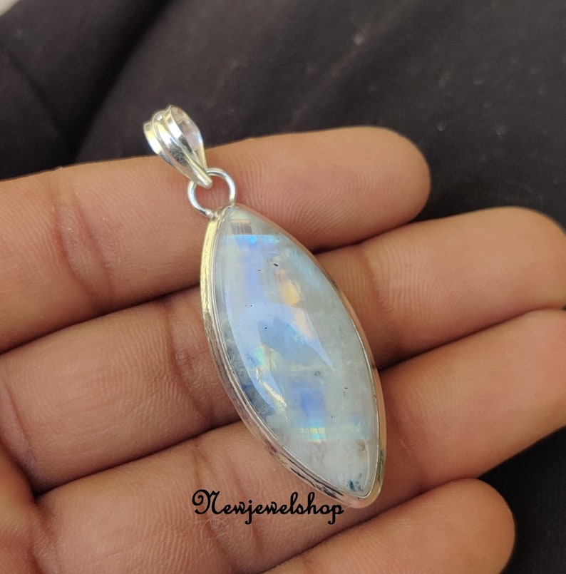 May include: A silver pendant featuring a large, oval-shaped moonstone with iridescent blue and white colours. The pendant has a simple, elegant design.