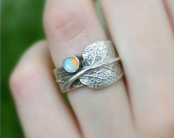 Puede incluir: Un anillo de plata con un diseño de hoja y una piedra preciosa de ópalo redonda en el centro.
