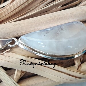 Puede incluir: Un colgante de plata con una piedra preciosa blanca opaca. El colgante tiene forma de l&aacute;grima y presenta un acabado liso y pulido. La piedra preciosa est&aacute; engastada en un engaste de plata y tiene un brillo sutil.