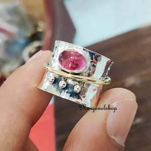 May include: A silver and gold spinning ring with a pink gemstone. The ring is hammered and has a textured surface.