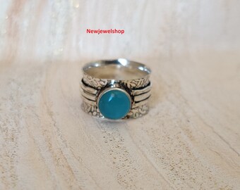 Può includere: Un anello d'argento con una pietra preziosa blu turchese e disegni floreali. L'anello è un anello girevole con una fascia testurizzata.