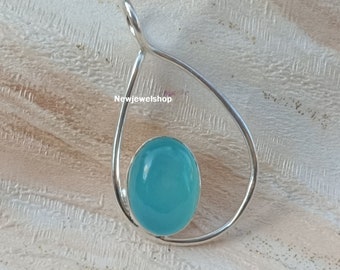 May include: A silver pendant featuring a light blue gemstone in a teardrop shape. The pendant is displayed on a white wooden surface.