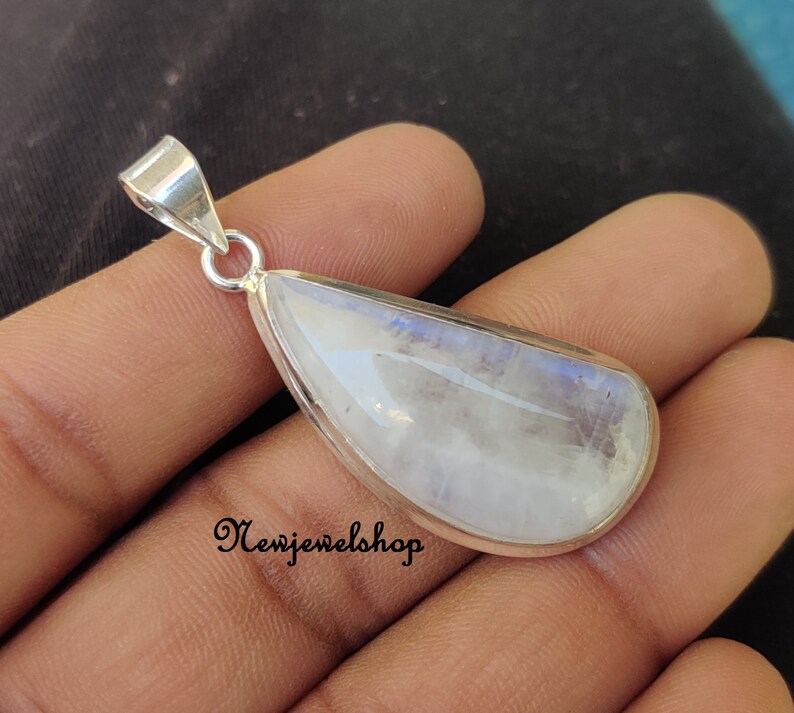 Puede incluir: Un colgante de piedra lunar en forma de l&aacute;grima engastado en plata de ley. La piedra es de color blanco lechoso con un brillo iridiscente azul.