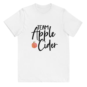May include: White t-shirt with black text that reads "Team Apple Cider" and a small red apple graphic.