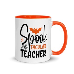 Puede incluir: Taza de caf&eacute; de cer&aacute;mica blanca con borde y asa naranja. La taza tiene un dise&ntilde;o en negro y naranja con el texto "Spooktacular Teacher" y una silueta de murci&eacute;lago.