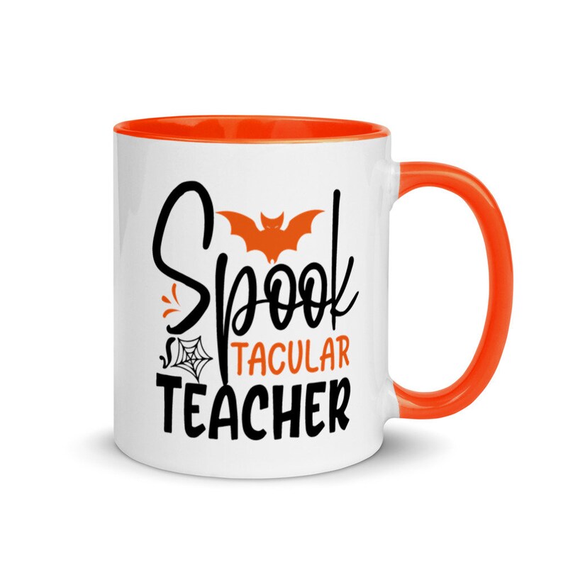 Puede incluir: Taza de caf&eacute; de cer&aacute;mica blanca con borde y asa naranja. La taza tiene un dise&ntilde;o en negro y naranja con el texto "Spooktacular Teacher" y una silueta de murci&eacute;lago.