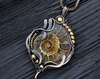 May include: A gold and copper wire wrapped pendant featuring a fossilized ammonite. The pendant is on a silver chain.
