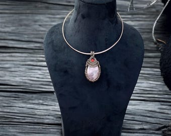 May include: A silver choker necklace with a pink and white oval pendant featuring a red gemstone. The pendant is wrapped in silver wire.
