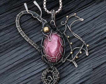 Puede incluir: Un colgante de alambre envuelto en plata y cobre con una piedra preciosa rosa, una forma de corazón y un pequeño diseño de caballo.