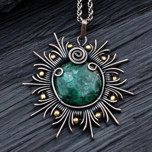 Può includere: Un ciondolo in pietra di malachite verde con un design a raggiera avvolto in filo d'argento e oro.