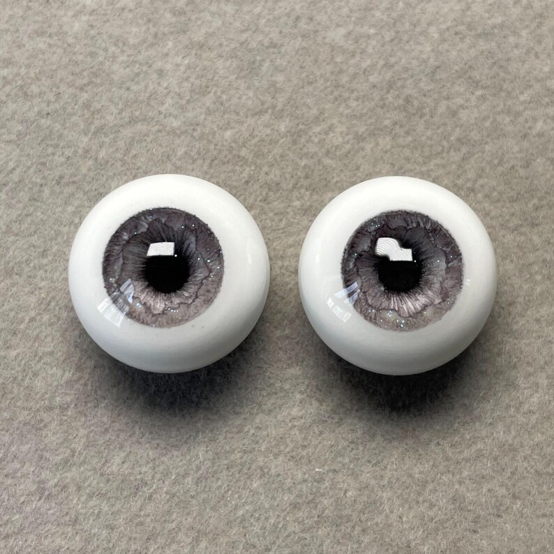 May include: Two gray and white doll eyes with a glitter finish. The irises are a dark gray with a black pupil.