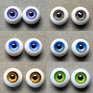 May include: Set of ten glass doll eyes in various colors, including purple, gray, blue, brown, and green. Each eye has a black pupil and a white sclera.