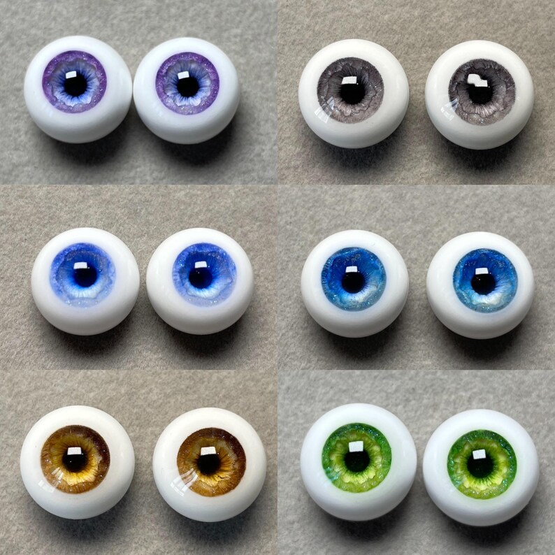 May include: Set of ten glass doll eyes in various colors, including purple, gray, blue, brown, and green. Each eye has a black pupil and a white sclera.