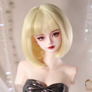 以下が含まれることがあります： 前髪のある短いストレートのブロンドボブヘアの、色白の球体関節人形。人形には、詳細に描かれた大きな茶色の目、はっきりとした眉、そしてペイントされた唇があります。光沢のあるダークグレーのストラップレスの衣服を着用しています。