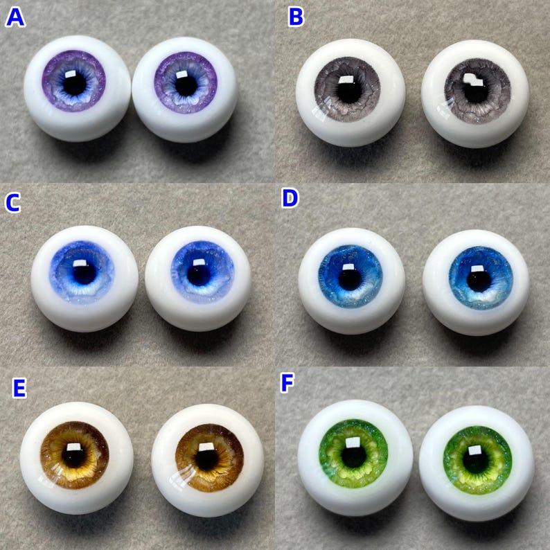 May include: Six pairs of glass doll eyes in various colors, including purple, gray, blue, brown, and green. Each pair is displayed on a white surface.