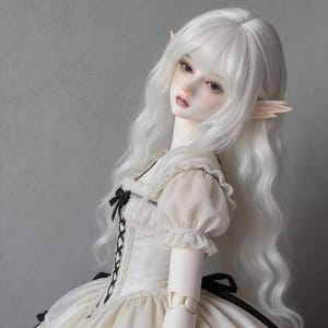 Puede incluir: Muñeca de porcelana con largo cabello blanco y rasgos delicados. La muñeca viste un vestido color crema con detalles negros, incluyendo un corpiño estilo corsé y un lazo. La muñeca tiene orejas puntiagudas y una expresión serena.