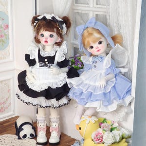 May include: Two porcelain dolls in frilly dresses. One doll wears a black and white maid outfit with a checkered bow. The other doll is in a blue and white dress with a matching bonnet. A panda figurine and a yellow duck figurine are at their feet.