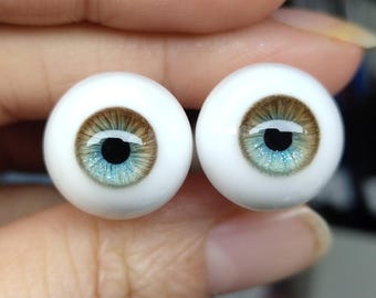 Puede incluir: Dos ojos de muñeca con esclerótica blanca, iris marrones y reflejos azul-verdosos. Las pupilas son negras y reflejan la luz. Estos ojos realistas están diseñados para muñecas u otros proyectos artísticos.