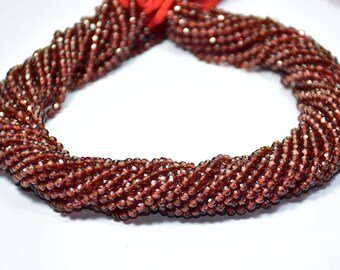 May include: A strand of dark red faceted gemstone beads. The beads are small and have a shiny, sparkly finish.