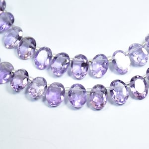 May include: A strand of oval-shaped amethyst beads, strung on a clear thread. The beads are a light purple colour and have a smooth, polished finish.