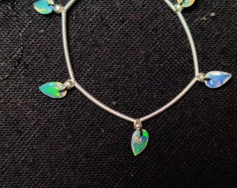 Può includere: Un braccialetto d'argento con cinque pietre di opale a forma di lacrima. Le pietre sono iridescenti con sfumature di verde, blu e bianco.