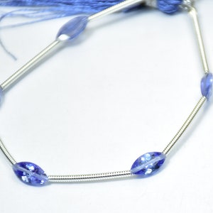 May include: A strand of blue gemstone beads on a silver chain. The beads are oval shaped and have a light blue colour.