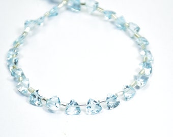 May include: A strand of light blue aquamarine gemstone beads, each bead is faceted and shaped like a triangle. The beads are strung on a silver wire.