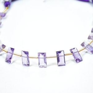 May include: A necklace featuring rectangular, light purple amethyst beads strung on a gold-colored wire. The beads are evenly spaced, and the necklace has a purple cord closure.