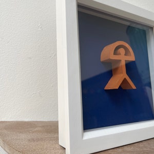 May include: A framed artwork featuring a 3D sculpture of a person with an umbrella, set against a dark blue background.