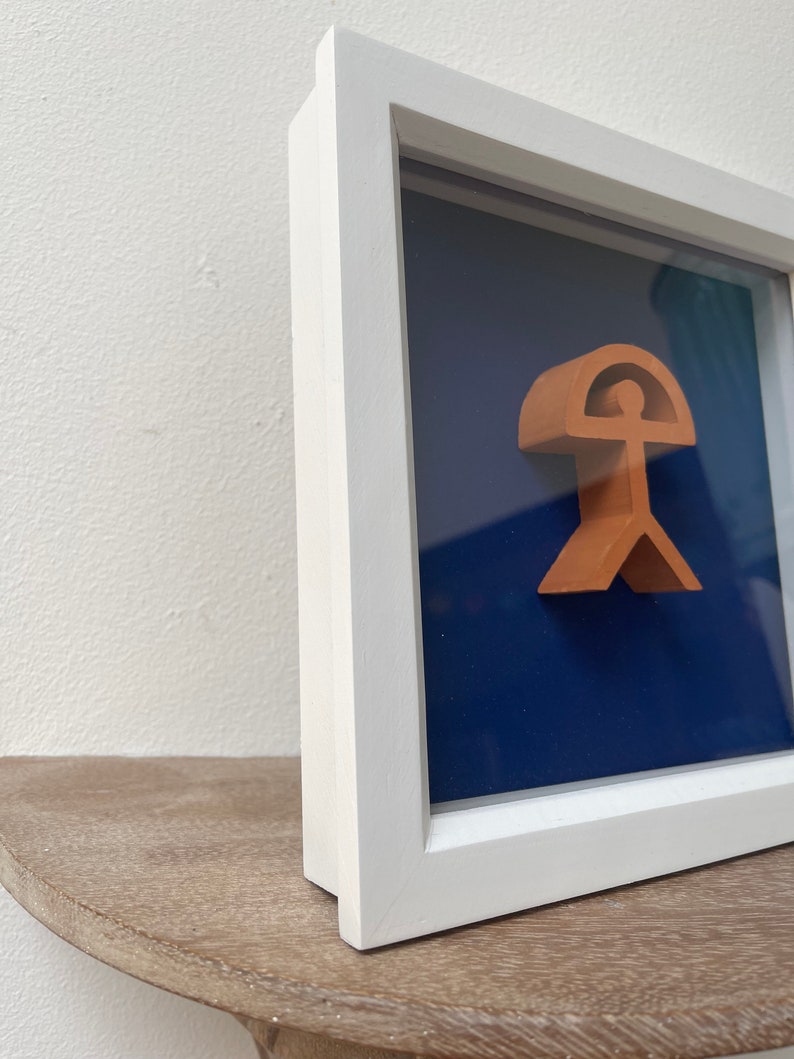 May include: A framed artwork featuring a 3D sculpture of a person with an umbrella, set against a dark blue background.