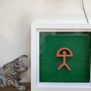 May include: A white framed picture with a green background and a brown symbol of a person with a circle above their head.