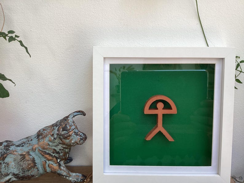 May include: A white framed picture with a green background and a brown symbol of a person with a circle above their head.