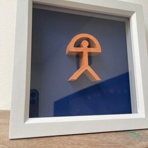 May include: A framed terracotta sculpture of a stylized human figure with a rounded top, set against a dark blue background.