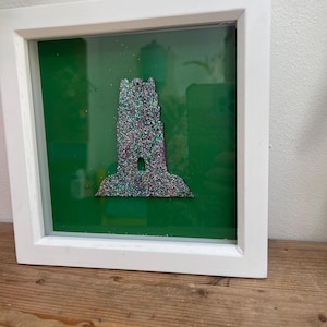 May include: A white frame with a green background and a glitter-covered tower silhouette.