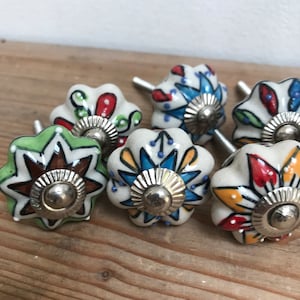 Könnte beinhalten: Sechs bunte Keramik-Schubladengriffe mit Stern- und Blumendesign. Jeder Griff hat eine silberne Metallbasis.