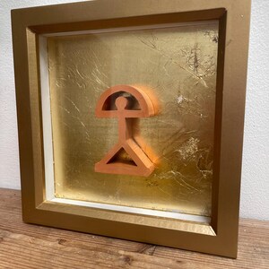 May include: A framed artwork featuring a three-dimensional, orange-colored geometric design against a gold leaf background.