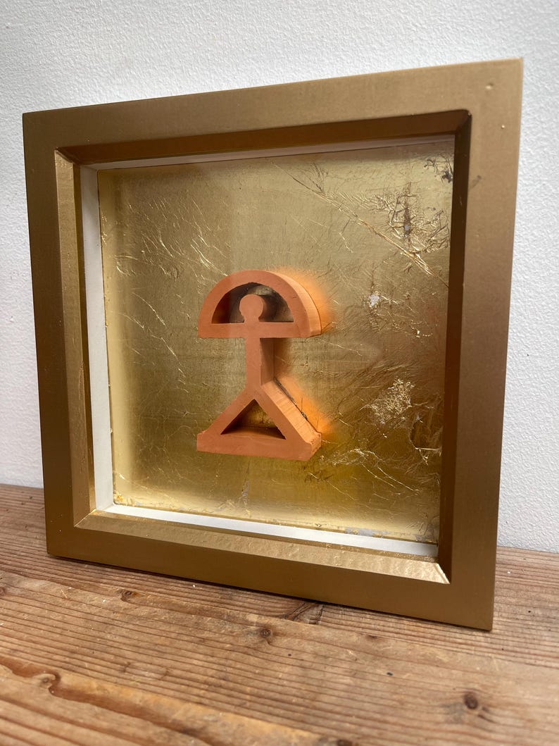 May include: A framed artwork featuring a three-dimensional, orange-colored geometric design against a gold leaf background.