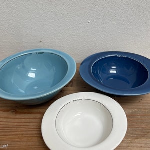 Op de afbeelding: Drie keramische kommen met maatstreepjes. De kommen zijn blauw, wit en lichtblauw. De kommen zijn gemarkeerd met "1 kop", "1/2 kop" en "1/4 kop".
