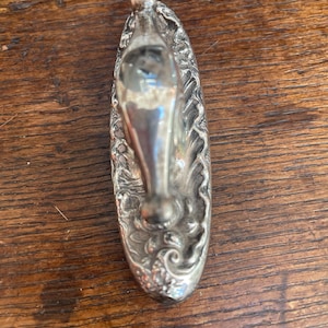 Op de afbeelding: Een zilverkleurige flesstopper met een sierlijk, bloemmotief. De stopper heeft een lange, slanke hals en een afgeronde bovenkant. Het ontwerp heeft ingewikkelde details en een gepolijste afwerking, geschikt voor wijnflessen.