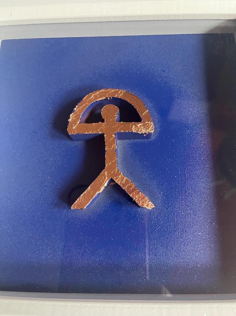 May include: A copper-colored stylized human figure with a rounded arch above its head, mounted on a dark blue background.