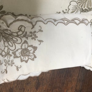 Op de afbeelding: Set witte linnen servetten met een delicaat geborduurd bloemenmotief in lichtbruine kleur. De servetten hebben een gegolfde rand.