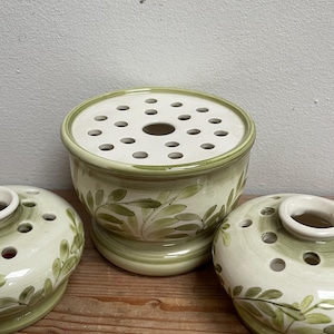 Könnte beinhalten: Drei Keramik-Blumenfrösche in einem hellgrünen und cremefarbenen Farbschema. Der größte Frosch hat die Form einer Schale mit einer perforierten Oberseite. Die anderen beiden sind kleinere, runde Formen. Alle haben ein gemaltes Blattdesign.