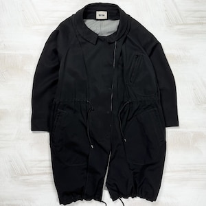 women's black polyamide coat featuring an oversized cyber techwear parka silhouette with utility drawstrings. The structured technical longline jacket with a collared neckline and asymmetrical zipper is displayed flat against a studio background, styled for a fluid cocoon fit corresponding to a clean size Large.