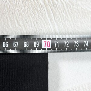 May include: A black fabric edge positioned against a black and white folding ruler. The ruler shows a measurement of 70 centimeters, with the black material aligned precisely at the 70-centimeter mark on the scale for accurate sizing.