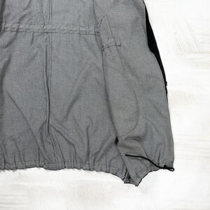 May include: A jacket interior featuring a fine black and white pinstripe lining. The garment includes a horizontal drawstring channel at the waist and a black drawstring cord with a toggle at the bottom hem, showcasing a structured inner construction.