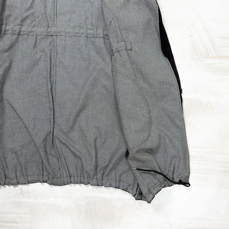 May include: A jacket interior featuring a fine black and white pinstripe lining. The garment includes a horizontal drawstring channel at the waist and a black drawstring cord with a toggle at the bottom hem, showcasing a structured inner construction.