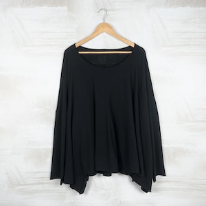 May include: A black long-sleeve top with a wide, flowing design. The top features a scoop neckline and is hanging on a wooden hanger against a white background.